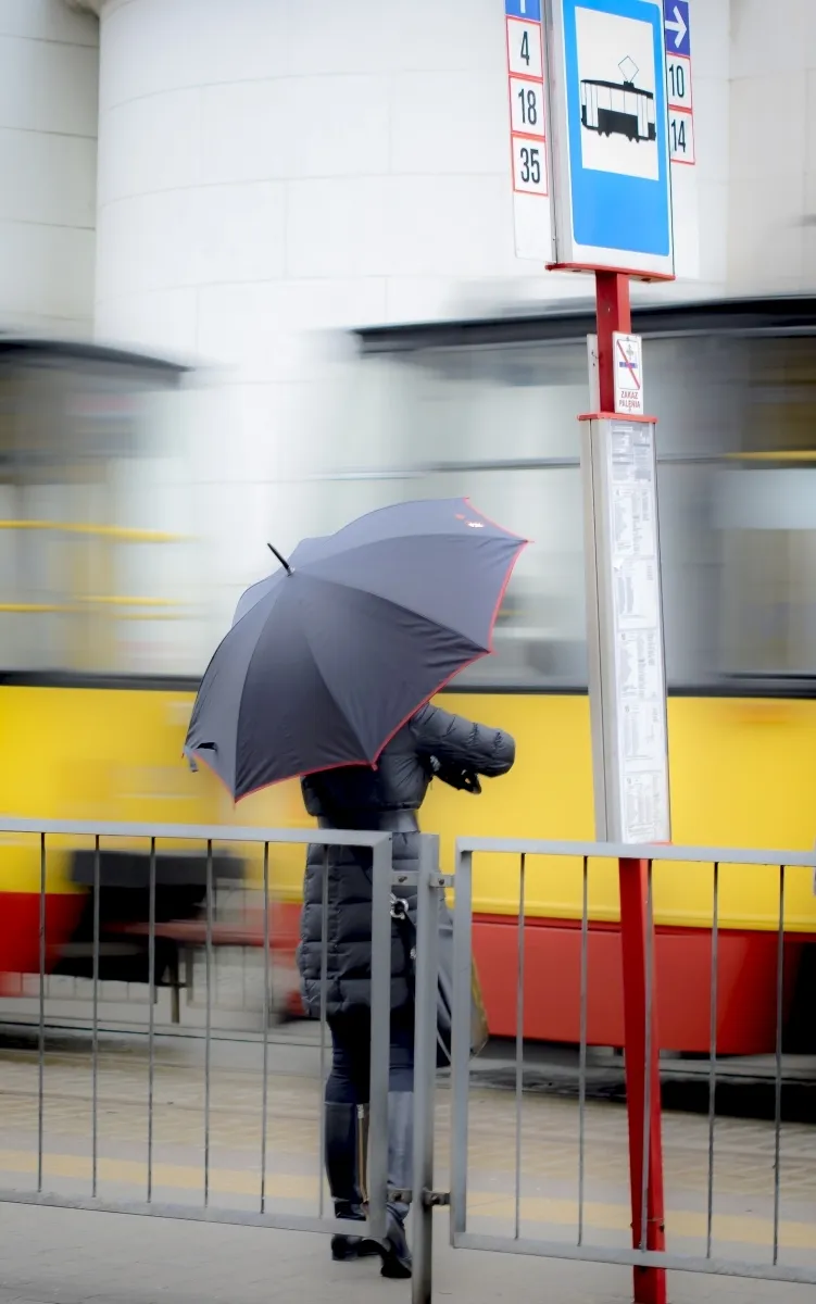 Dark umbrella silhouette beside a yellow tram and bus stop sign
